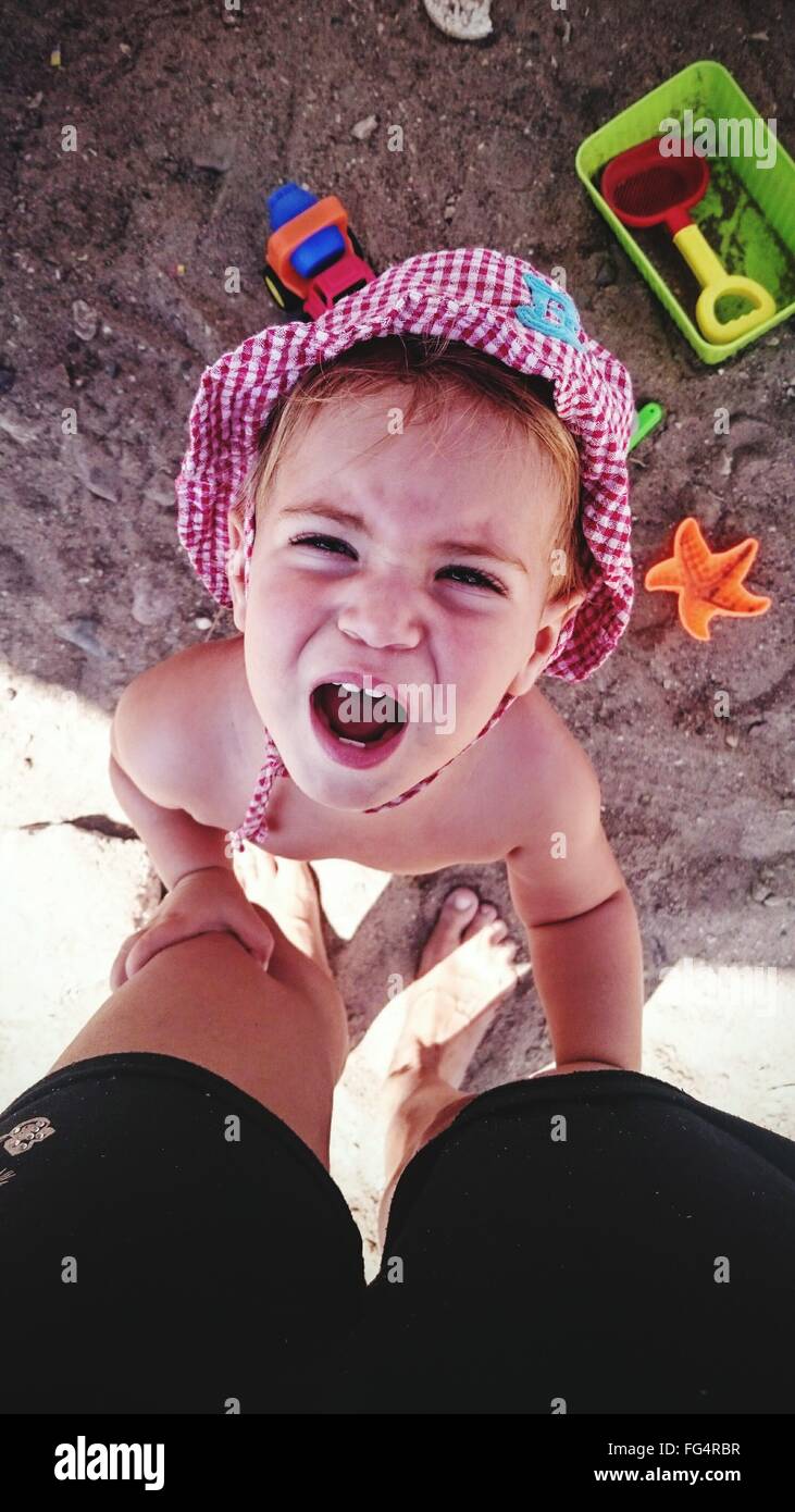 Directly Above Shot Of Girl Crying While Holding Father's Legs At Beach Stock Photo