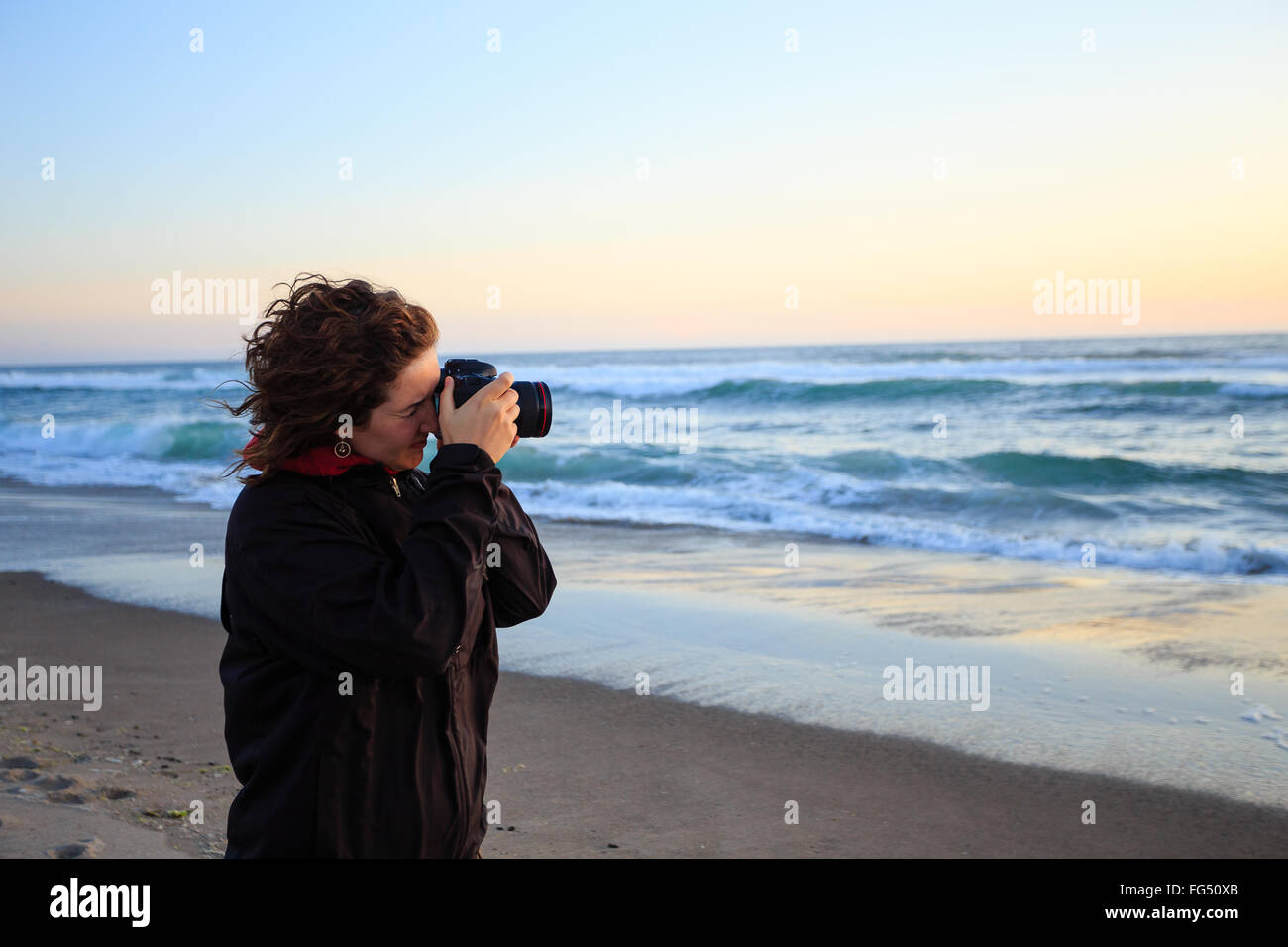 Sunset photos being shot by a woman with a camera on the beach at dusk. Stock Photo