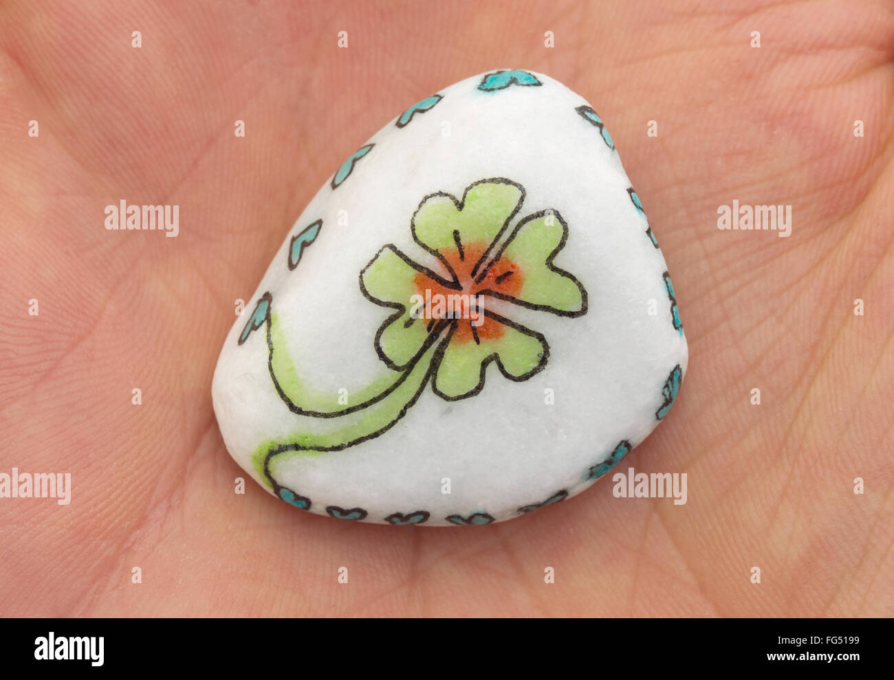 Stone with drawing of a clover four and small hearts, isolated on a hand Stock Photo