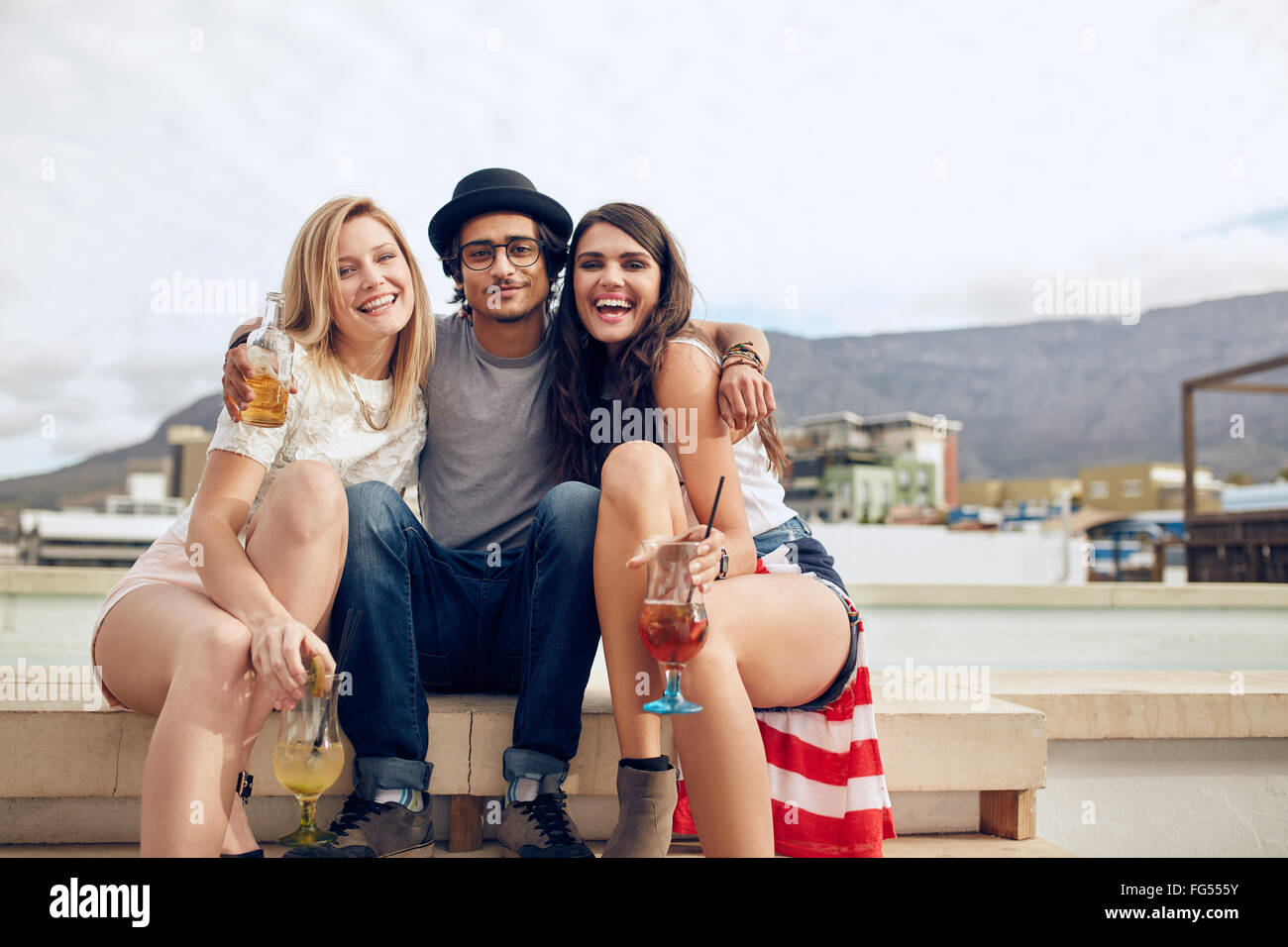 Portrait of best friends hanging out on a roof with drinks. Young man and women partying outdoors. Stock Photo