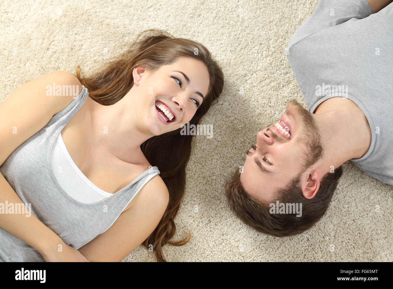 Happy couple laughing looking each other and lying on a carpet at home Stock Photo
