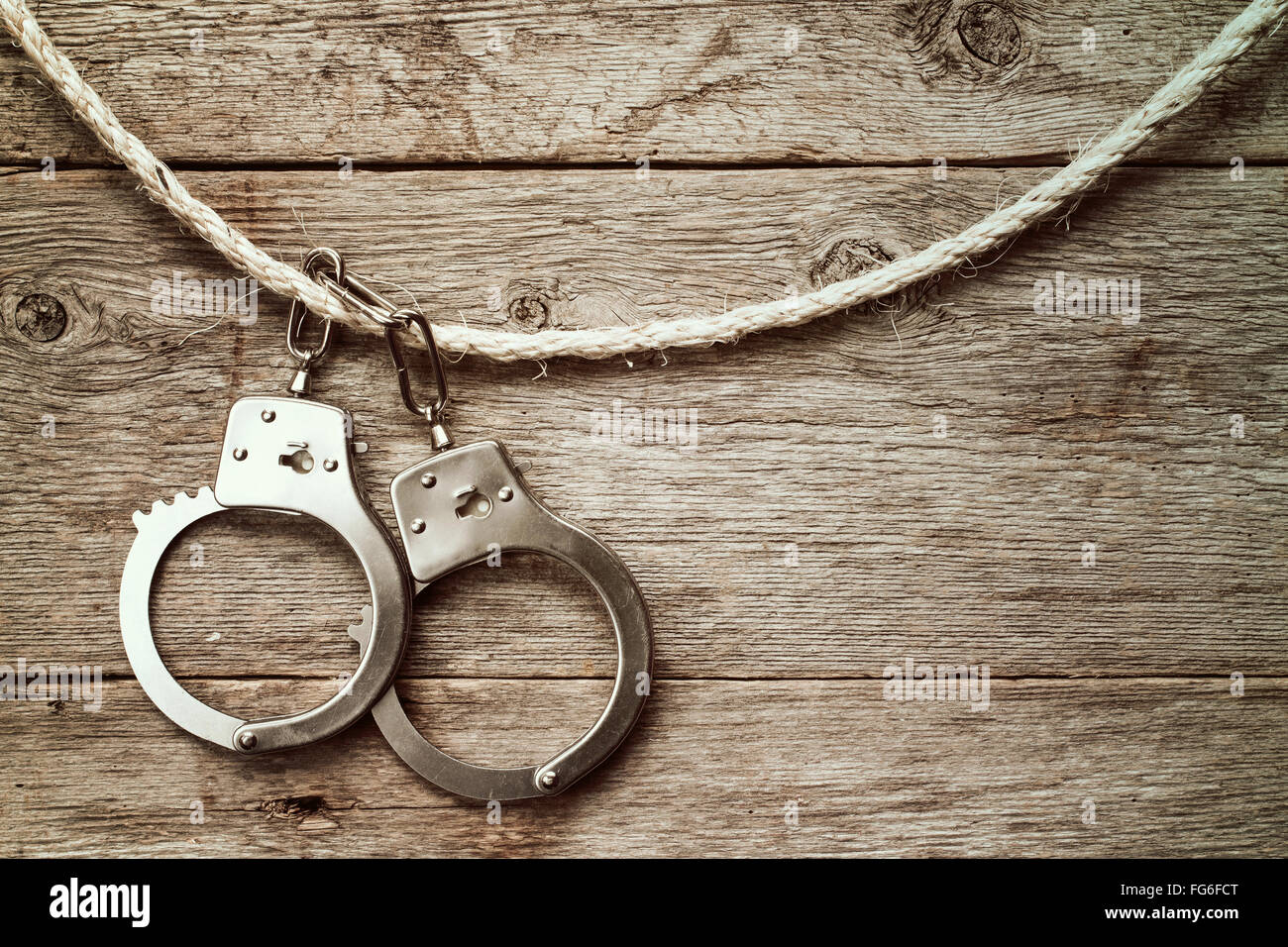 Handcuffs hanging on the rope against old wooden wall. Stock Photo