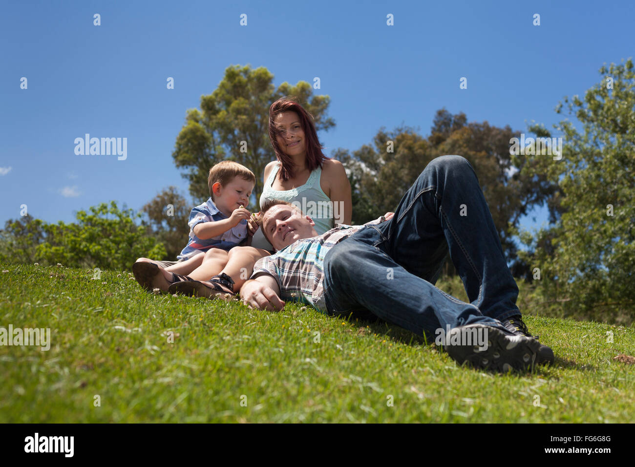 Young happy family relaxing in the grass and enjoying summer day outdoors. Stock Photo