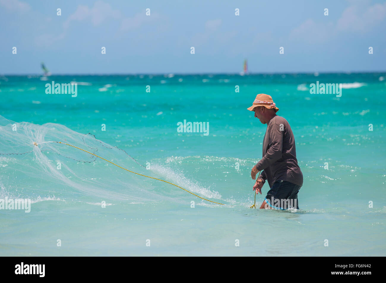 A Cuban male fisherman casts a net in the Caribbean sea to catch fish in the blue water on a sunny day; Varadero, Cuba Stock Photo