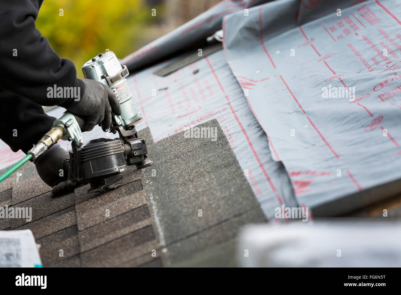 Close up of air nailer, with male roofer nailing new shingles on top of