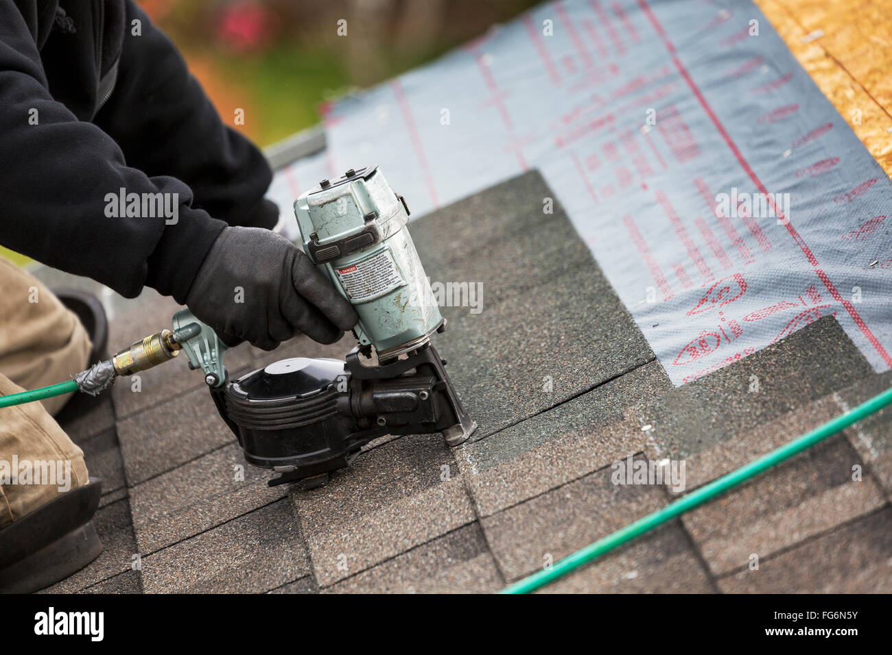 Close up of air nailer, with male roofer nailing new shingles on top of