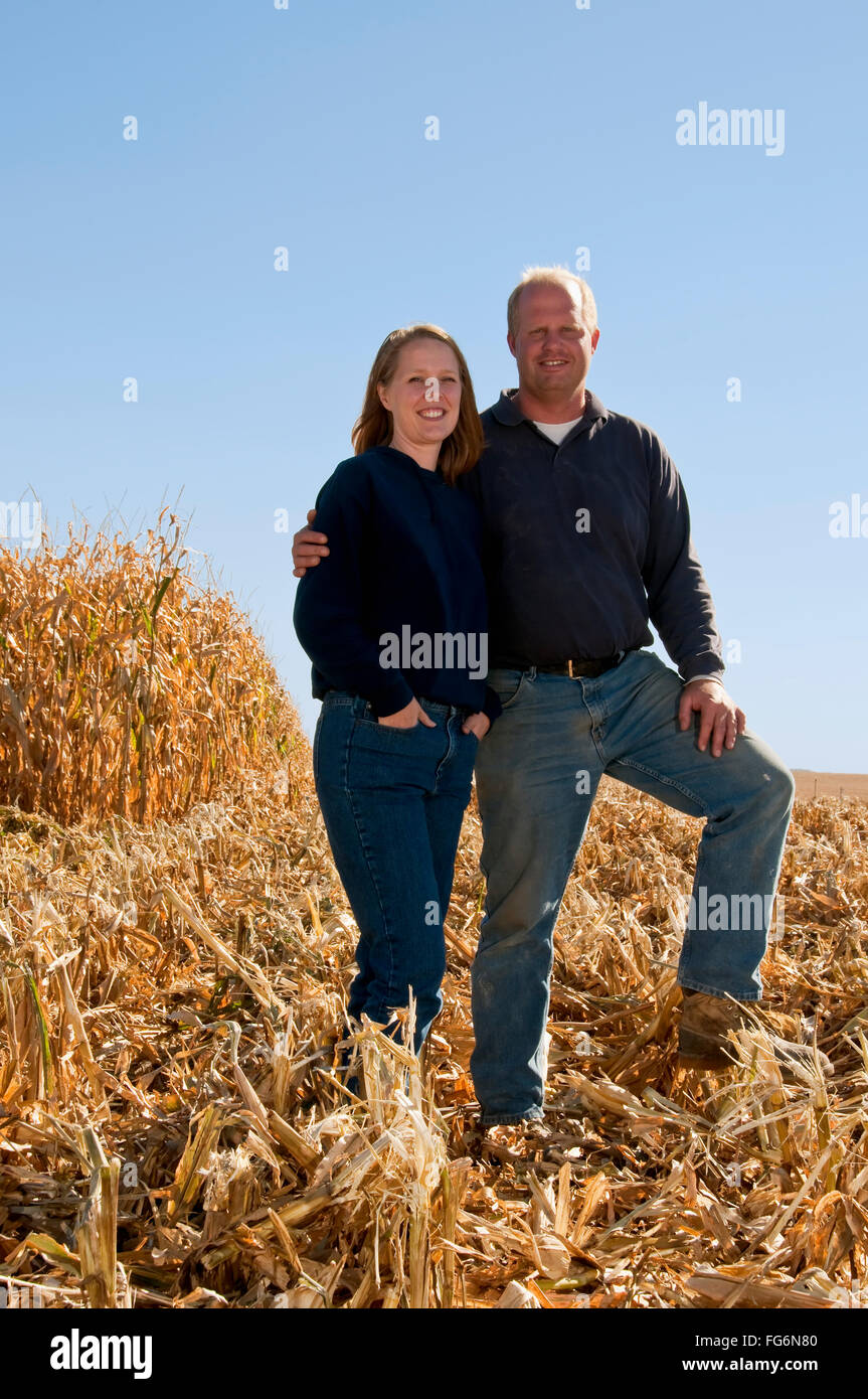 Agriculture - Farmer husband and wife pose together in a partially harvested grain corn field in Autumn / near Sioux City, Iowa, USA. Stock Photo