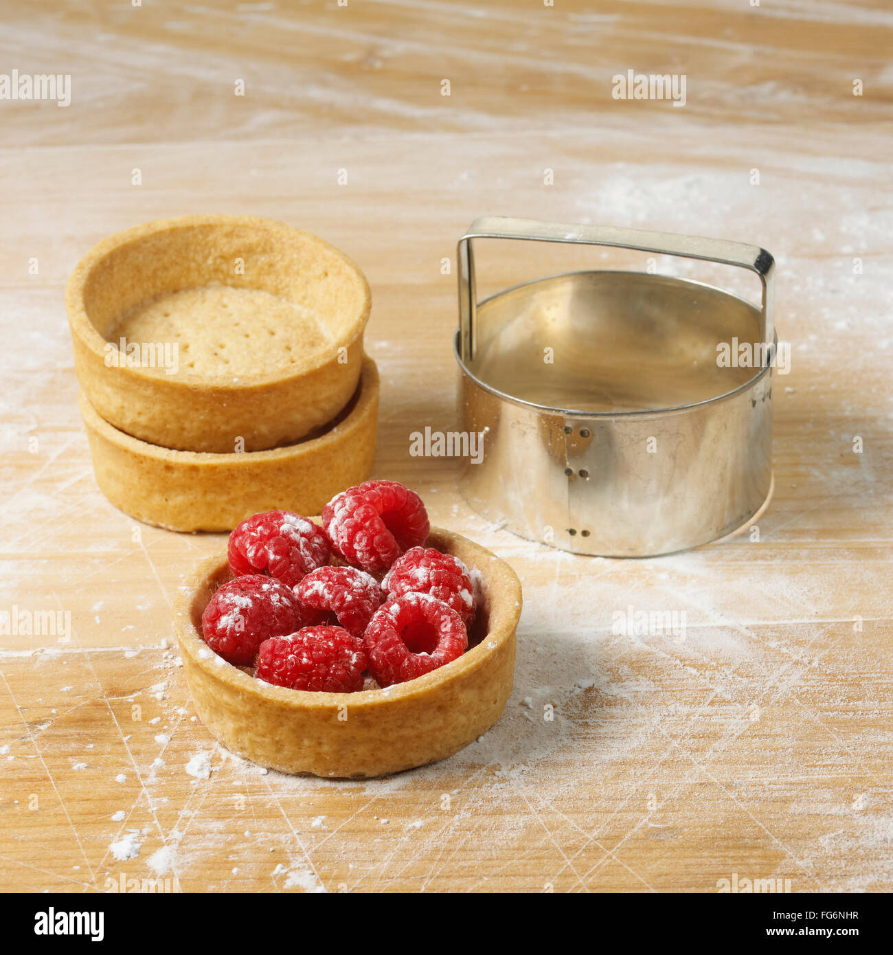 Dessert cups on a floured surface with raspberries in one, and a round