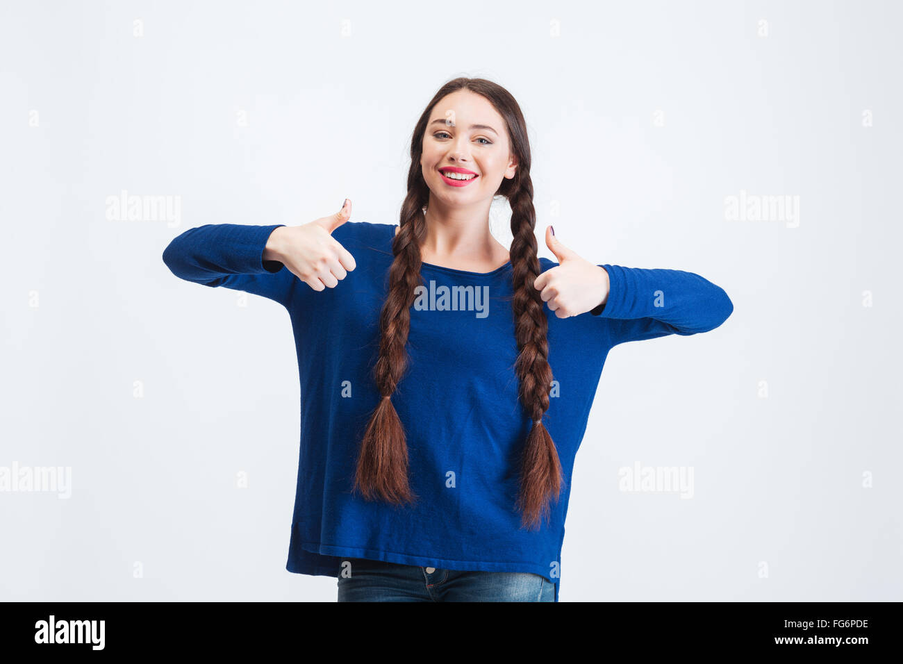Beautiful happy young woman with two braids standing and showing thumbs up with both hands over white background Stock Photo