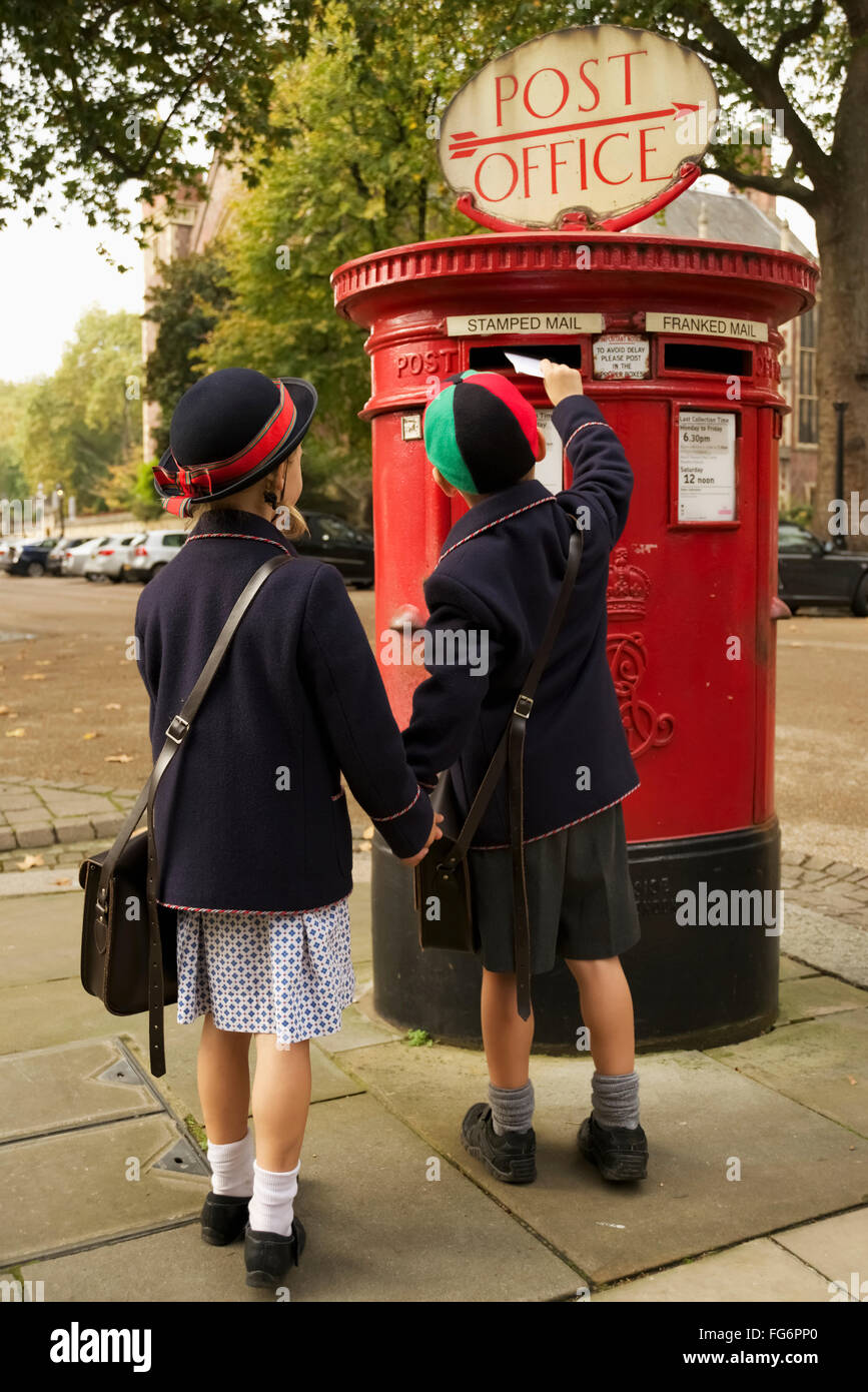Brother and sister holding hands posting letter; London, England Stock