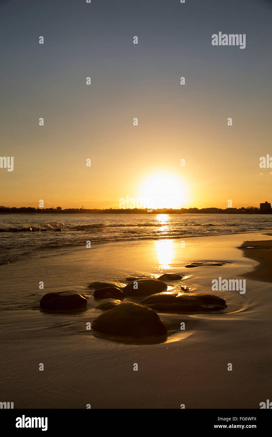 A golden sun sets over the horizon and reflects on the wet beach along the coast; Caloundra, Queensland, Australia Stock Photo