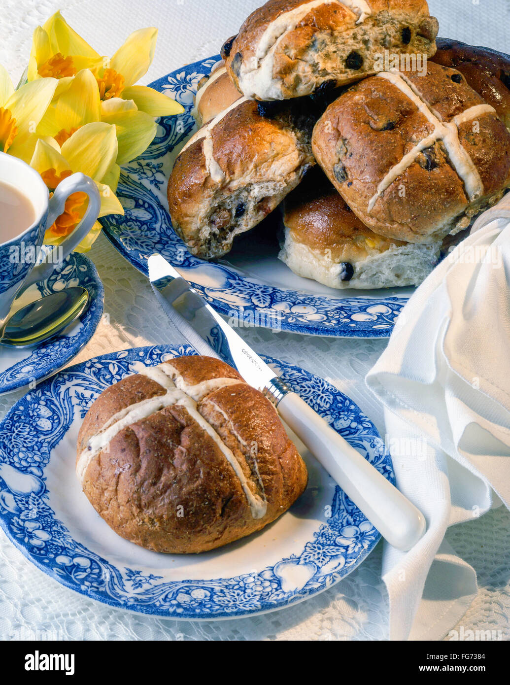 Hot cross buns on plate ith knife and cup of tea in studio setting Stock Photo
