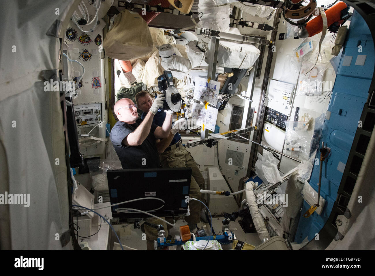 NASA astronaut Scott Kelly and ESA astronaut Timothy Peake (right) review images during a procedure to replace a fan pump separator inside one of the  spacesuits in the Quest Airlock aboard the International Space Station February 10, 2016 in Earth Orbit. Stock Photo