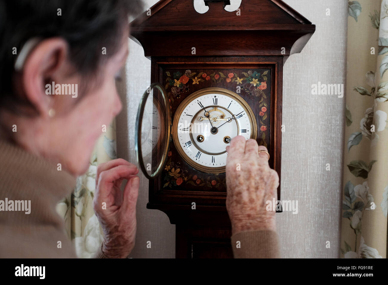 Elderly lady winding up her antique Grandaughter Clock in her dining room at home putting time