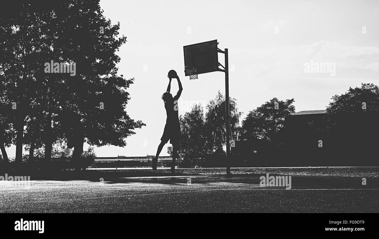 Man Playing Basketball By Trees Against Sky Stock Photo