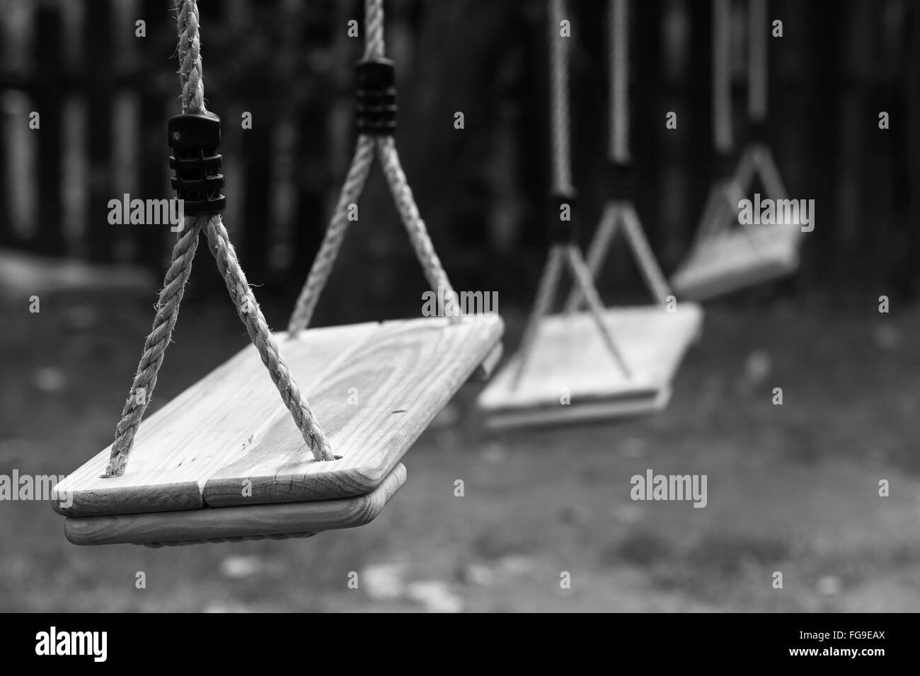 Horizontal perspective view of three wooden child swings in the park with shallow depth of field Stock Photo