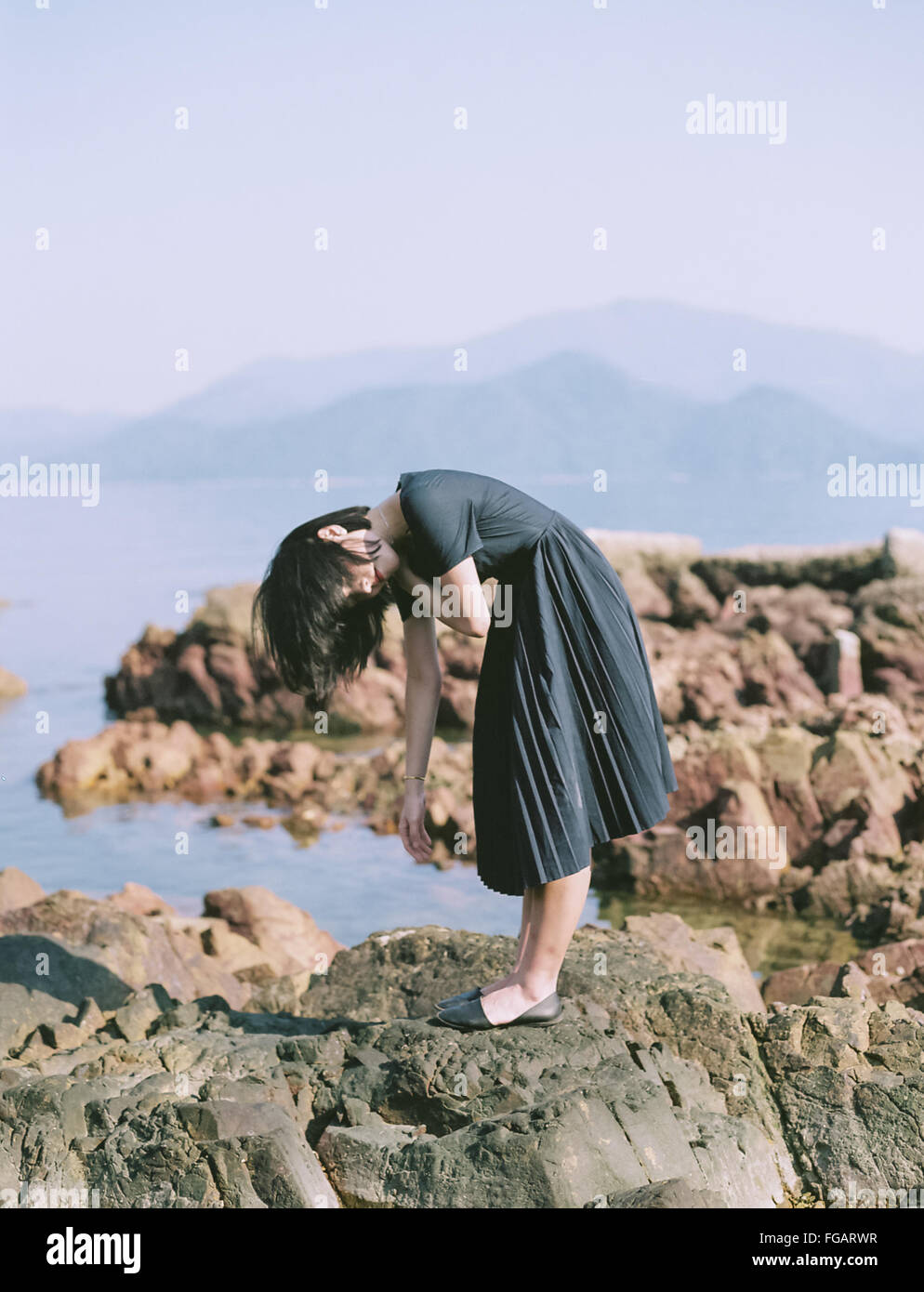 Woman Bending While Standing On Rock At Seaside Stock Photo