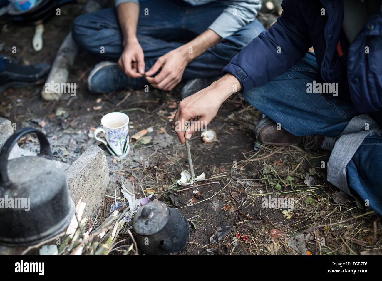 The hands of Kurdish refugees as they boil water in a kettle over a fire by their tent in the jungle refugee camp, Calais. Stock Photo