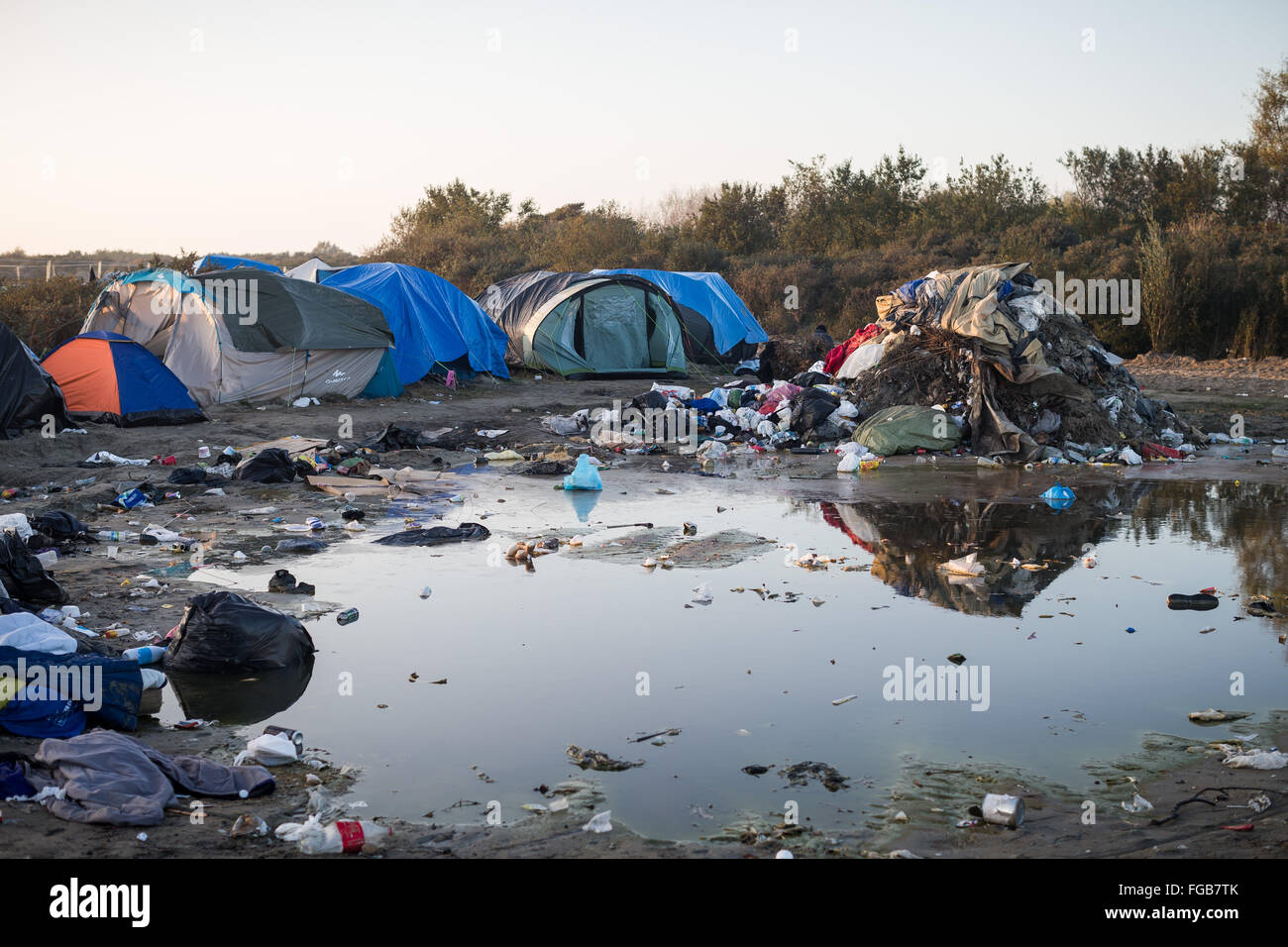 Rubbish accumulates next to a large puddle in the muddy environment of the Jungle Refugee Camp in Calais, France. Stock Photo