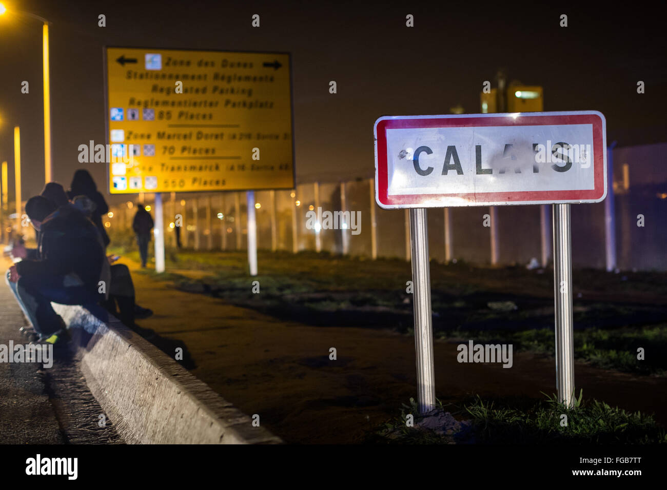 Refugees wait into the night by a Calais road sign before they leave to make an attempt at crossing into the UK via the tunnel. Stock Photo