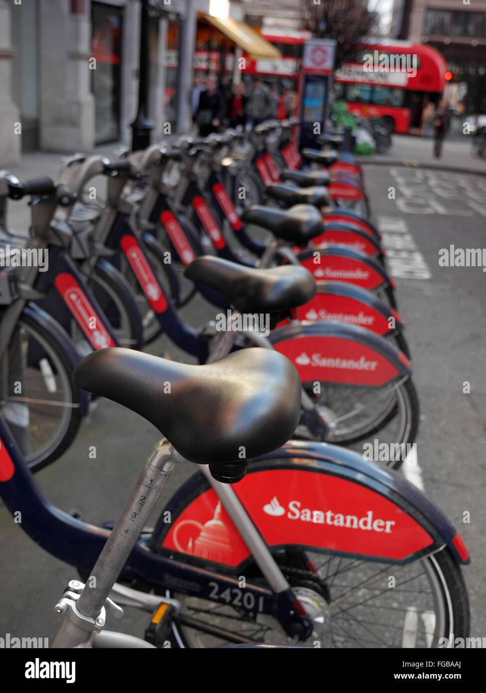 TFL London red Santander rental hire bikes bicycles in Covent Garden with sponsor livery of Santander red London Bus in background  London UK Stock Photo