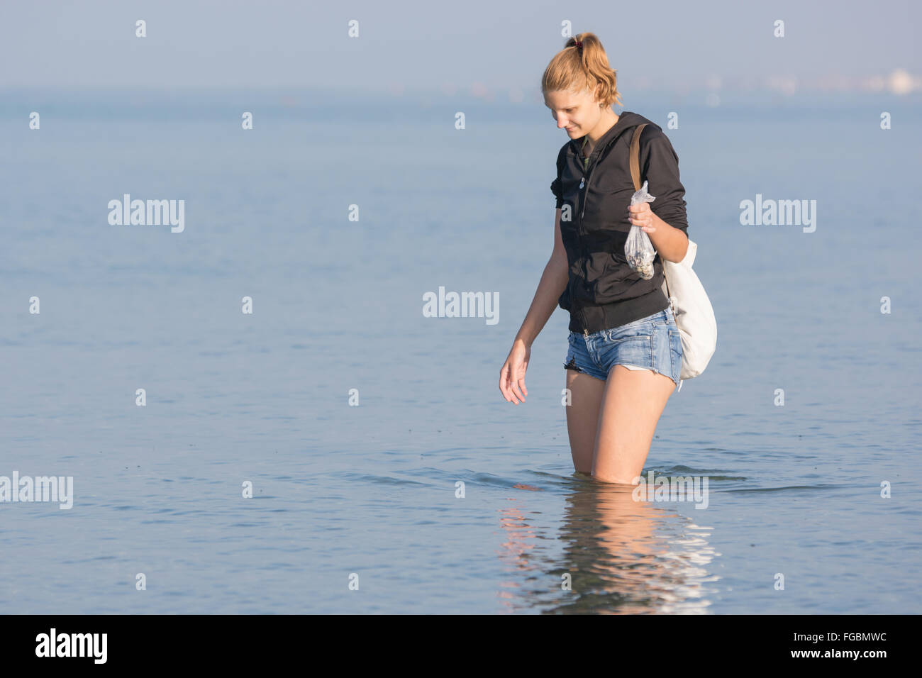 Young girl collecting seashells on the sea early in the morning and puts in a bag Stock Photo