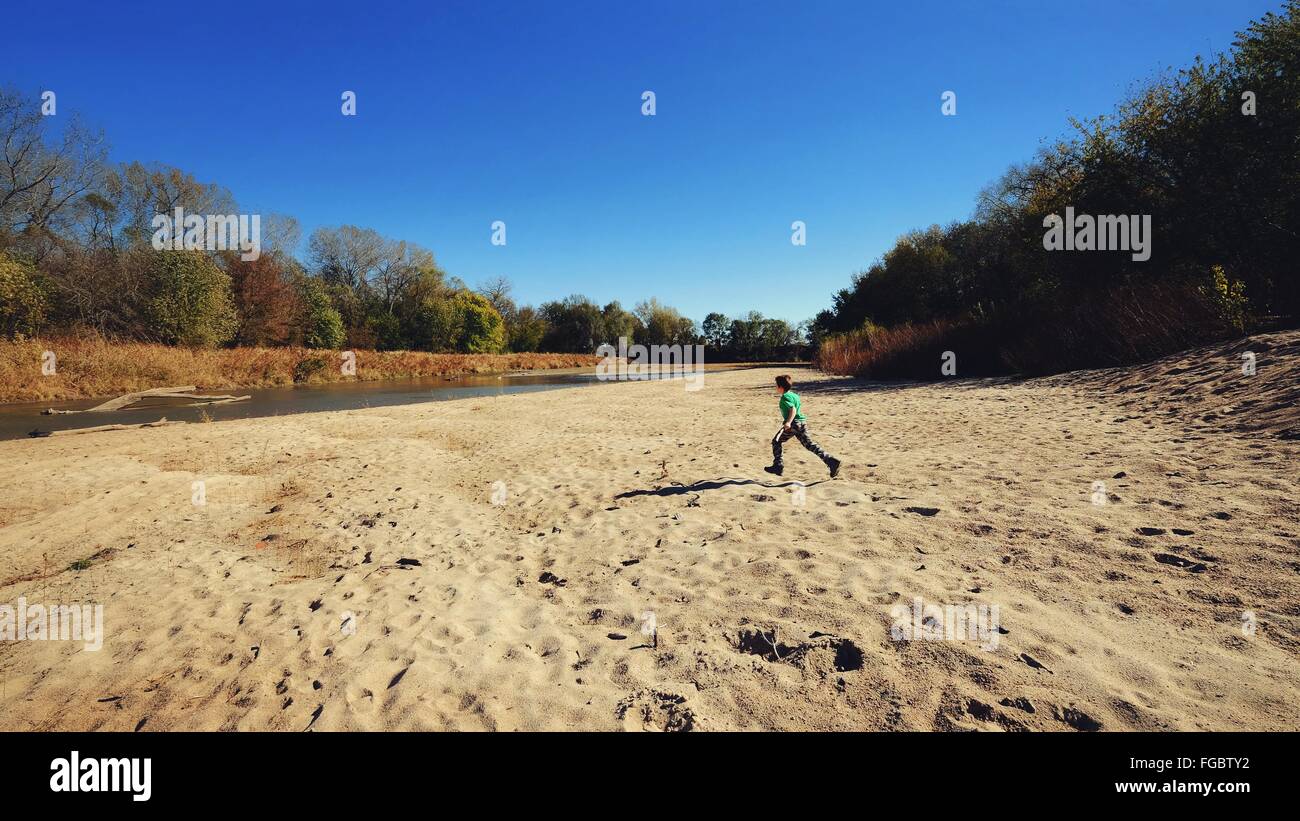Boy Running On Sand At Little Blue River Against Sky Stock Photo