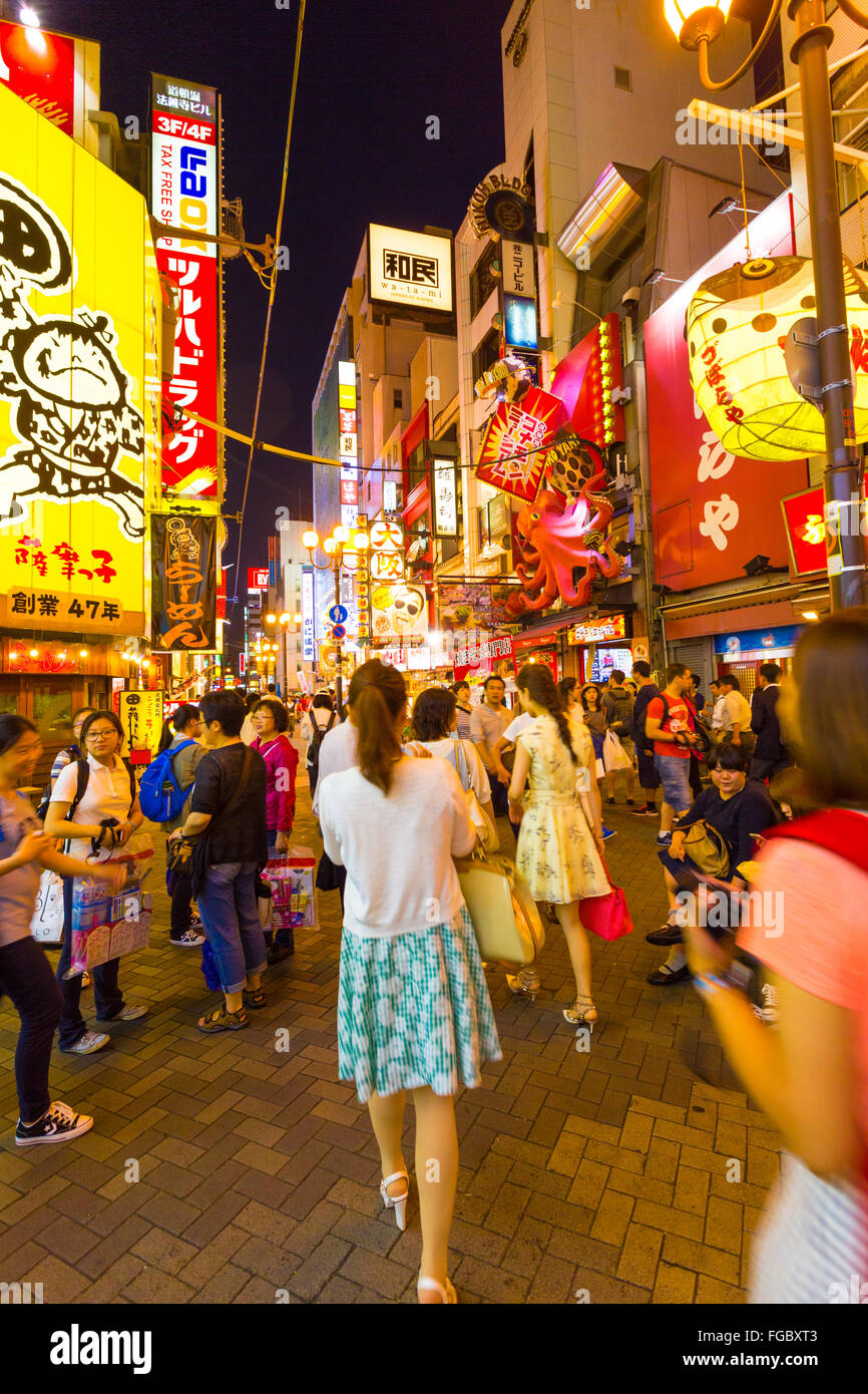 Tourists walking around crowded and busy Dotombori Arcade amid bright neon signs and lights, the center of nightlife at night in Stock Photo