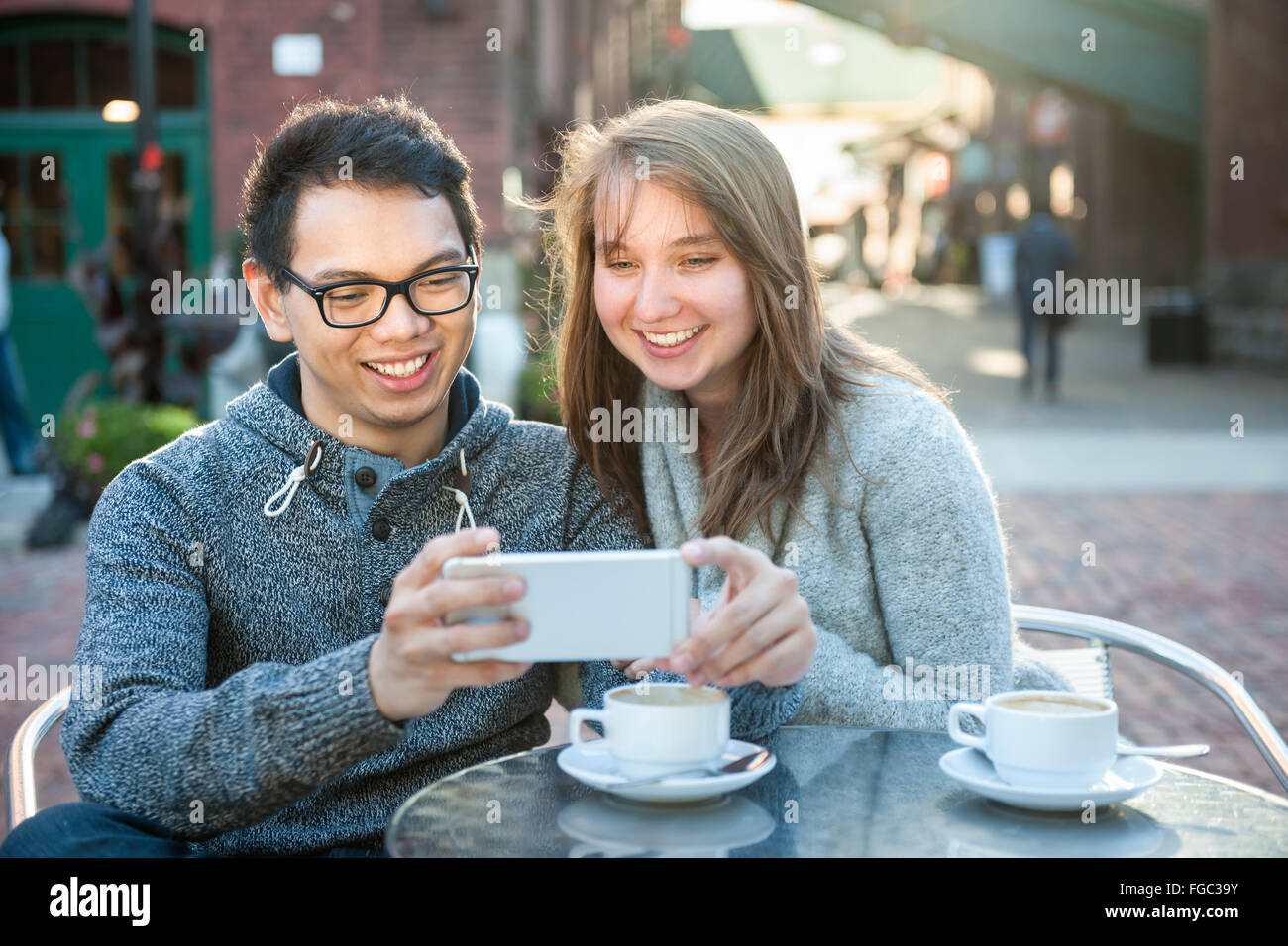 Two young people looking into smartphone on outdoor cafe patio Stock Photo