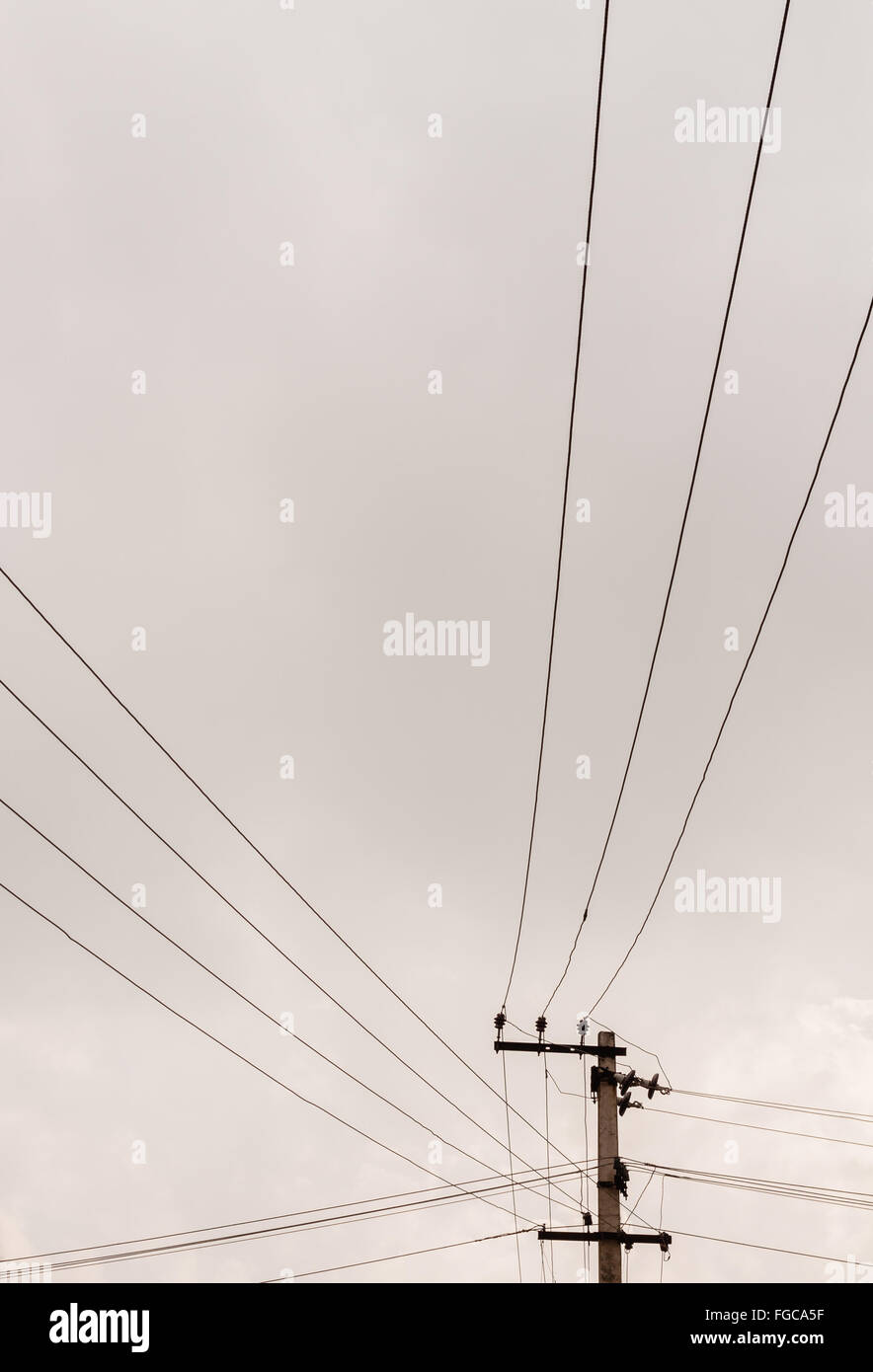 Power transmission lines from a transmission pole run across the sky covered with dark grey rain clouds. Stock Photo