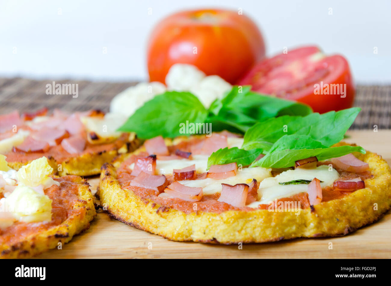 Closeup of small round baked pizza made of cauliflower crust and topped with bacon, ham, halloumi cheese, lountza, tomato sauce  Stock Photo