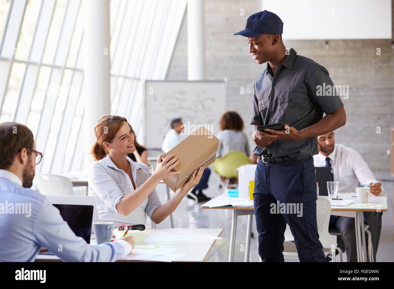 Courier Delivering Package To Businesswoman In Busy Office Stock Photo