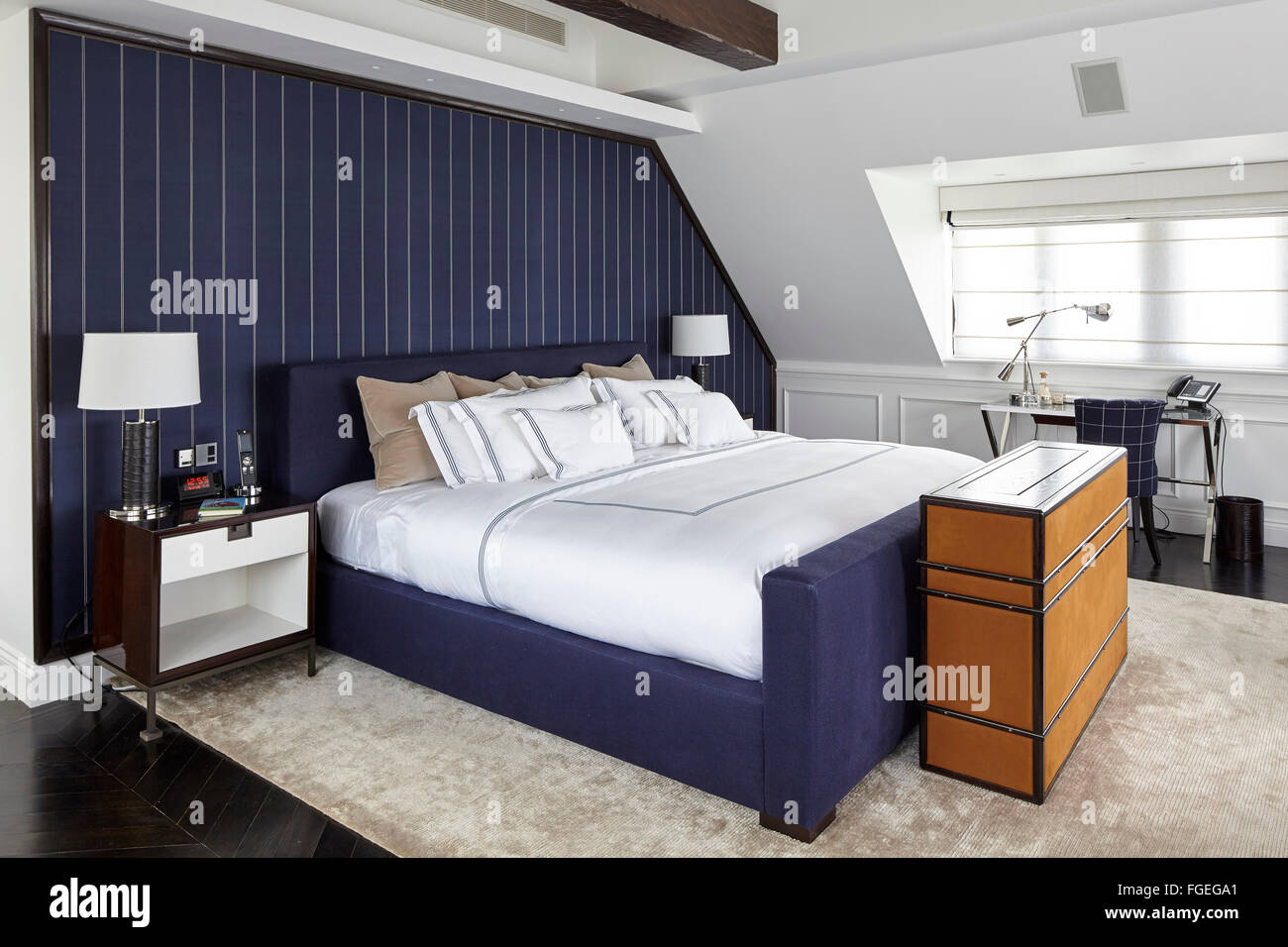 Master bedroom with dark blue pinstripe fabric wall covering with TV cabinet at end of bed and desk under window. Tudor Hall, Po Stock Photo