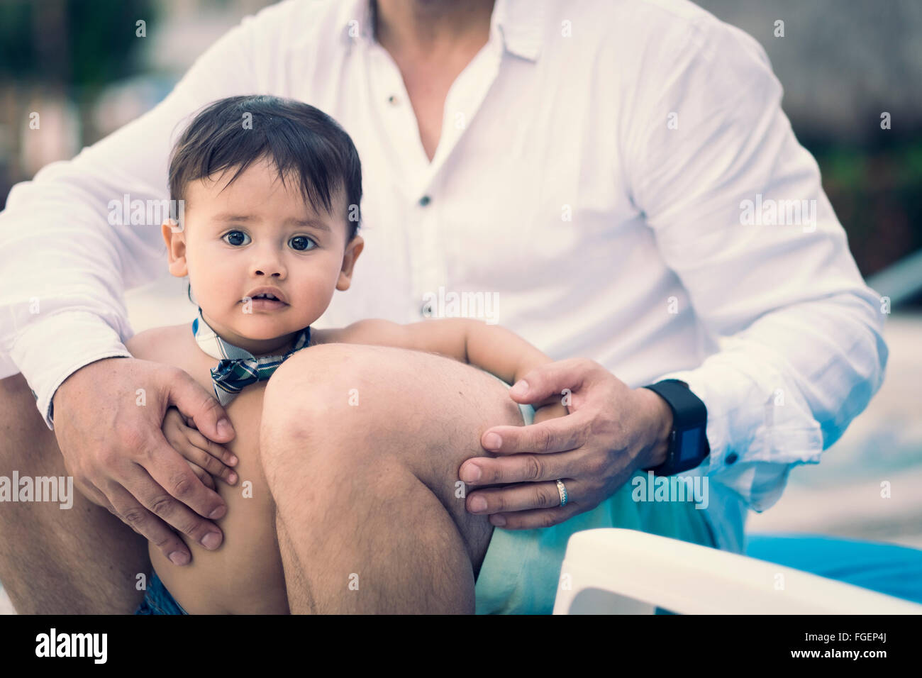 Male hispanic child, 1 year of age, held by his father between his legs Stock Photo