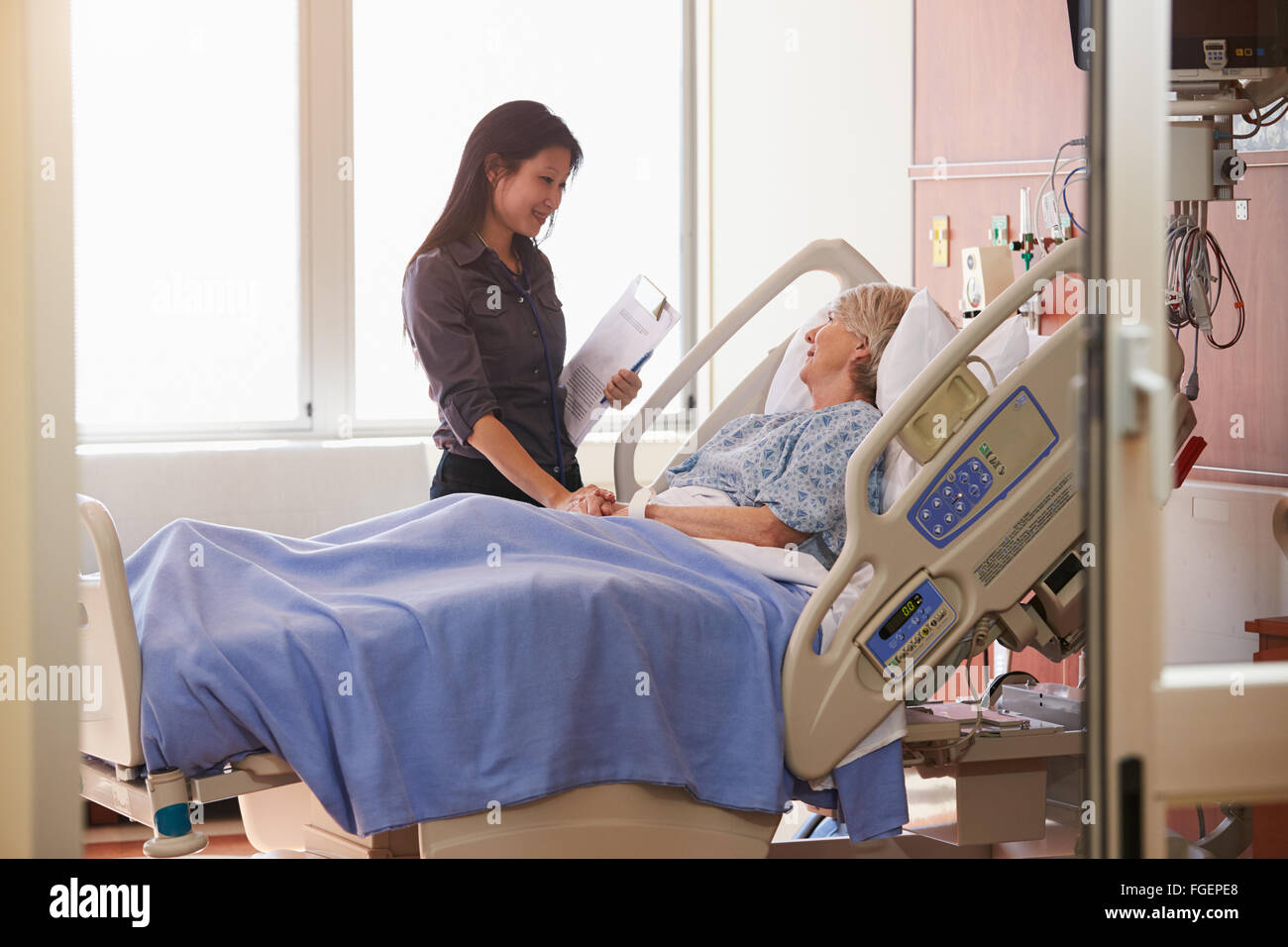 Female Doctor Talks To Senior Female Patient In Hospital Bed Stock Photo