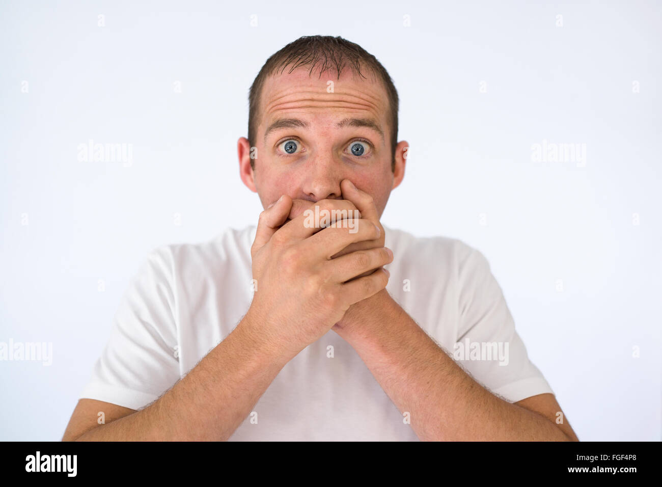 Man with his hands covering his mouth looking shocked Stock Photo