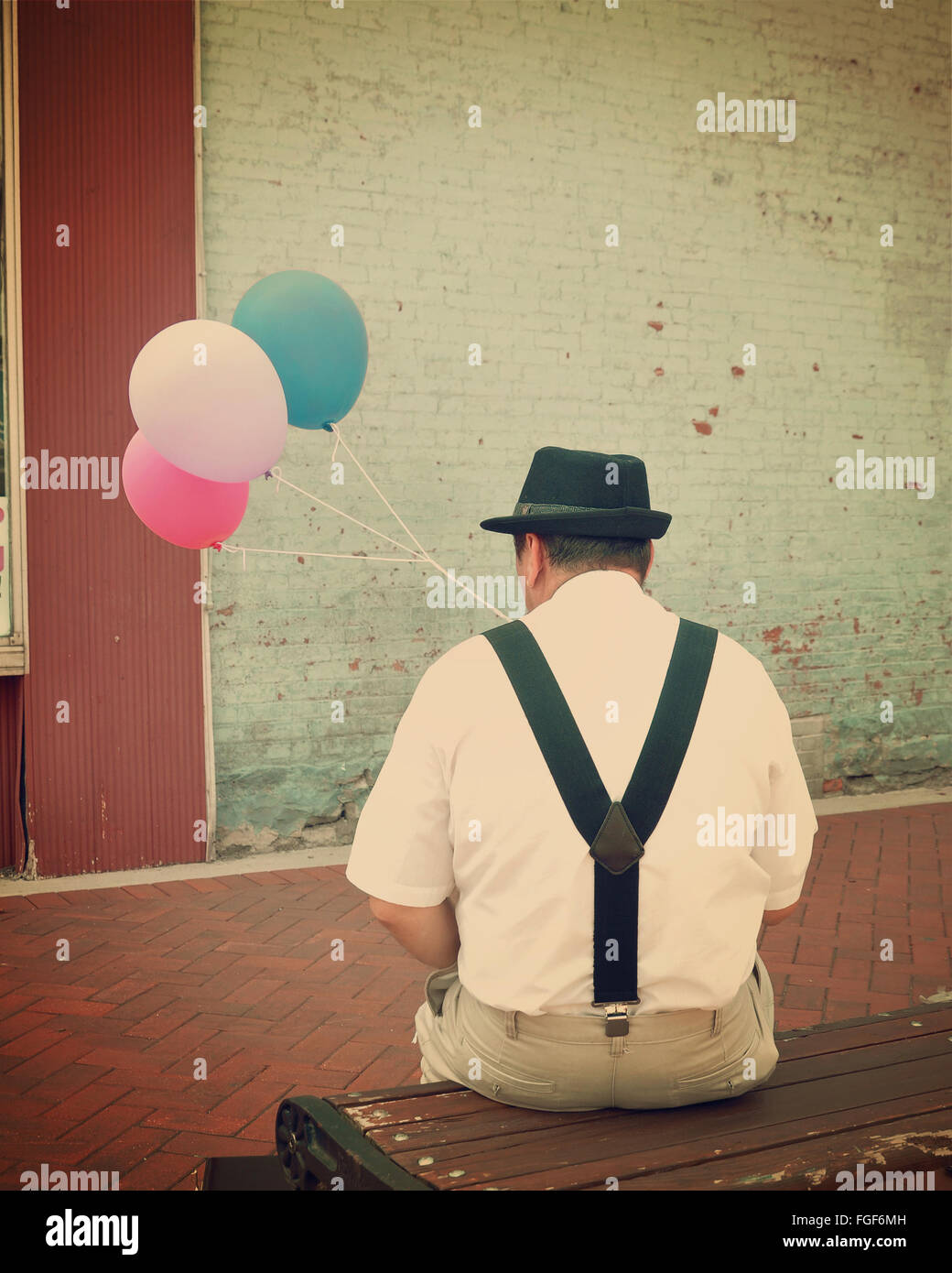 A vintage retro business man is sitting on a bench downtown with colorful balloons for a happiness or creativity concept. Stock Photo