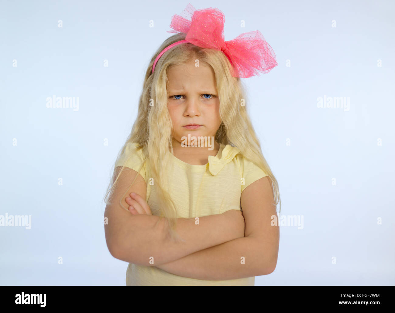 Young girl with long blonde hair and folded arms, frowning with a sad and grumpy expression Stock Photo