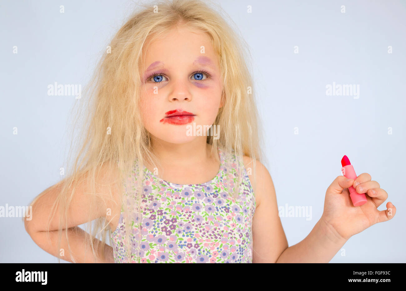 Young girl with blonde hair wearing smudged make up holding a red lipstick Stock Photo