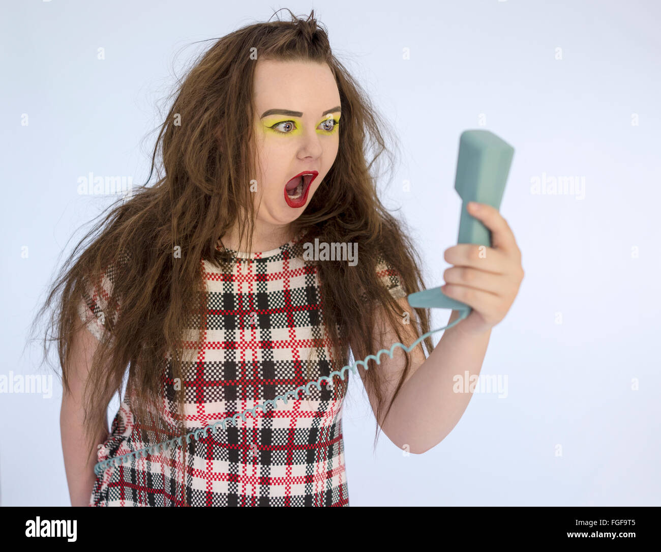 Teenage girl screaming at a blue retro telephone handset in her hand Stock Photo