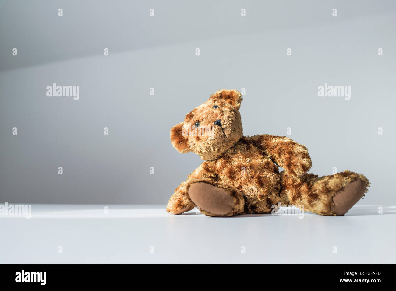 Brown teddy bear sitting on the floor leaning to one side Stock Photo