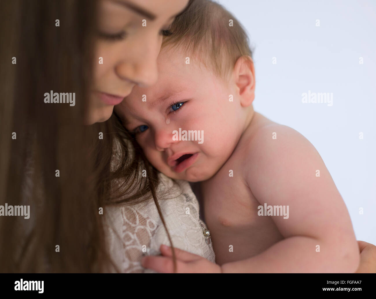 Mother holding baby son in arms crying with a single tear emerging from his eye Stock Photo