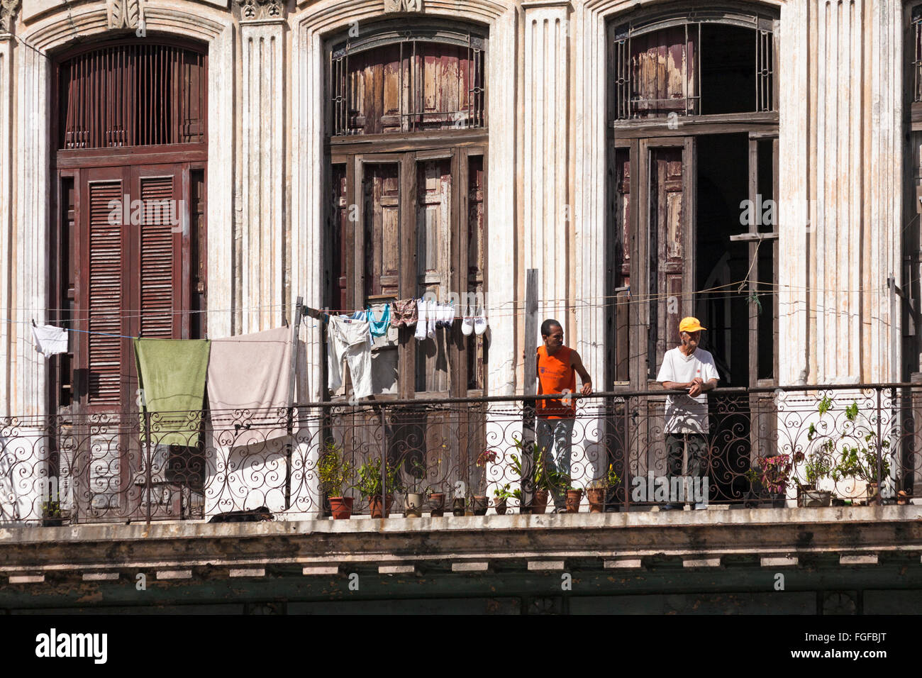 Daily life in Cuba - Cuban men leaning on balcony railings with washing hung out to dry at Havana, Cuba, West Indies, Caribbean, Central America Stock Photo