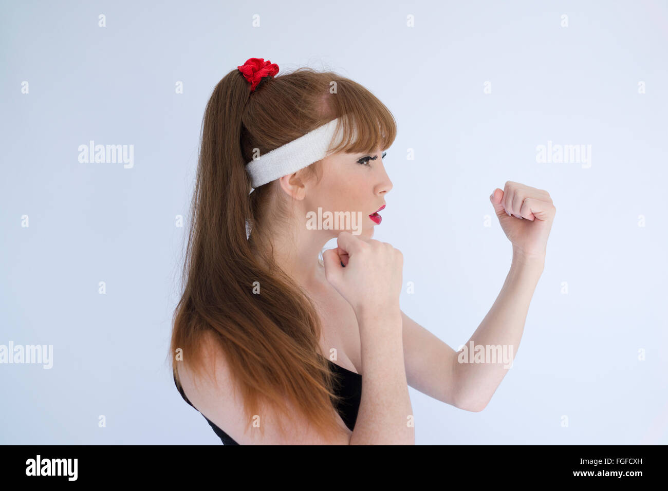 Woman with long brown hair wearing a head sweatband with her fists clenched preparing to engage in boxing Stock Photo