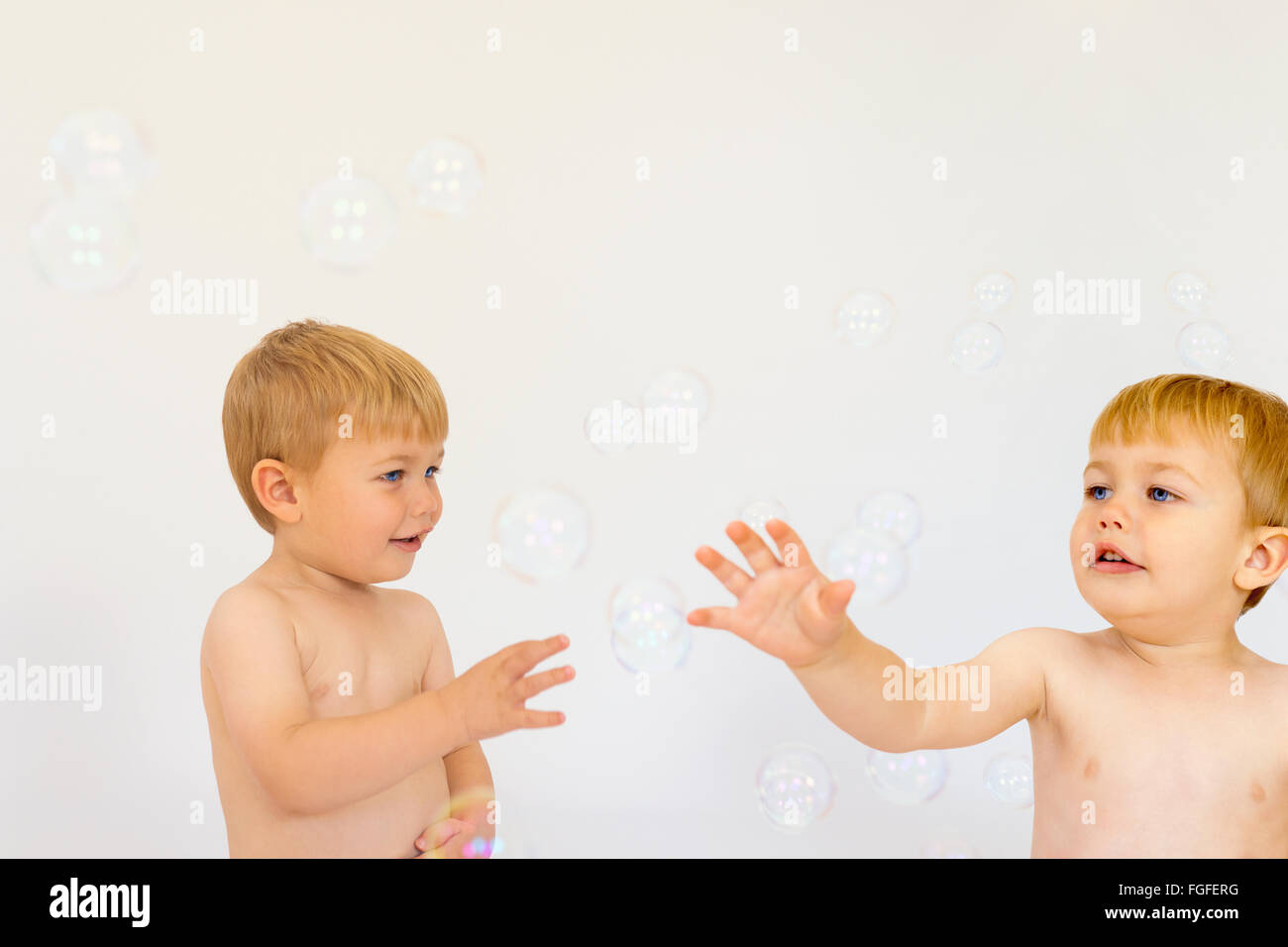Identical twin boys reaching out to touch bubbles floating in the air Stock Photo