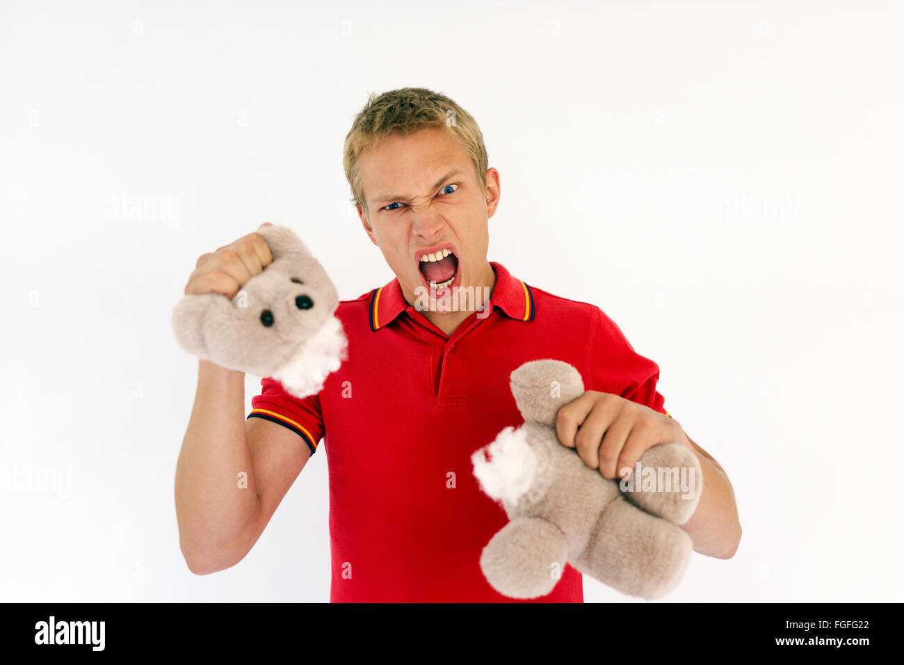 Man ripping the head off a cute cuddly toy teddy bear screaming in a moment of anger Stock Photo