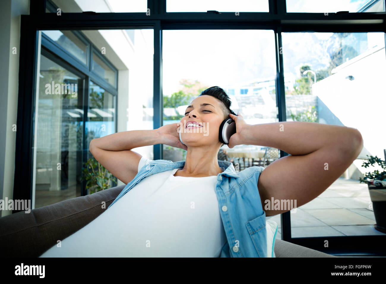 Pregnant woman listening to music on sofa Stock Photo - Alamy