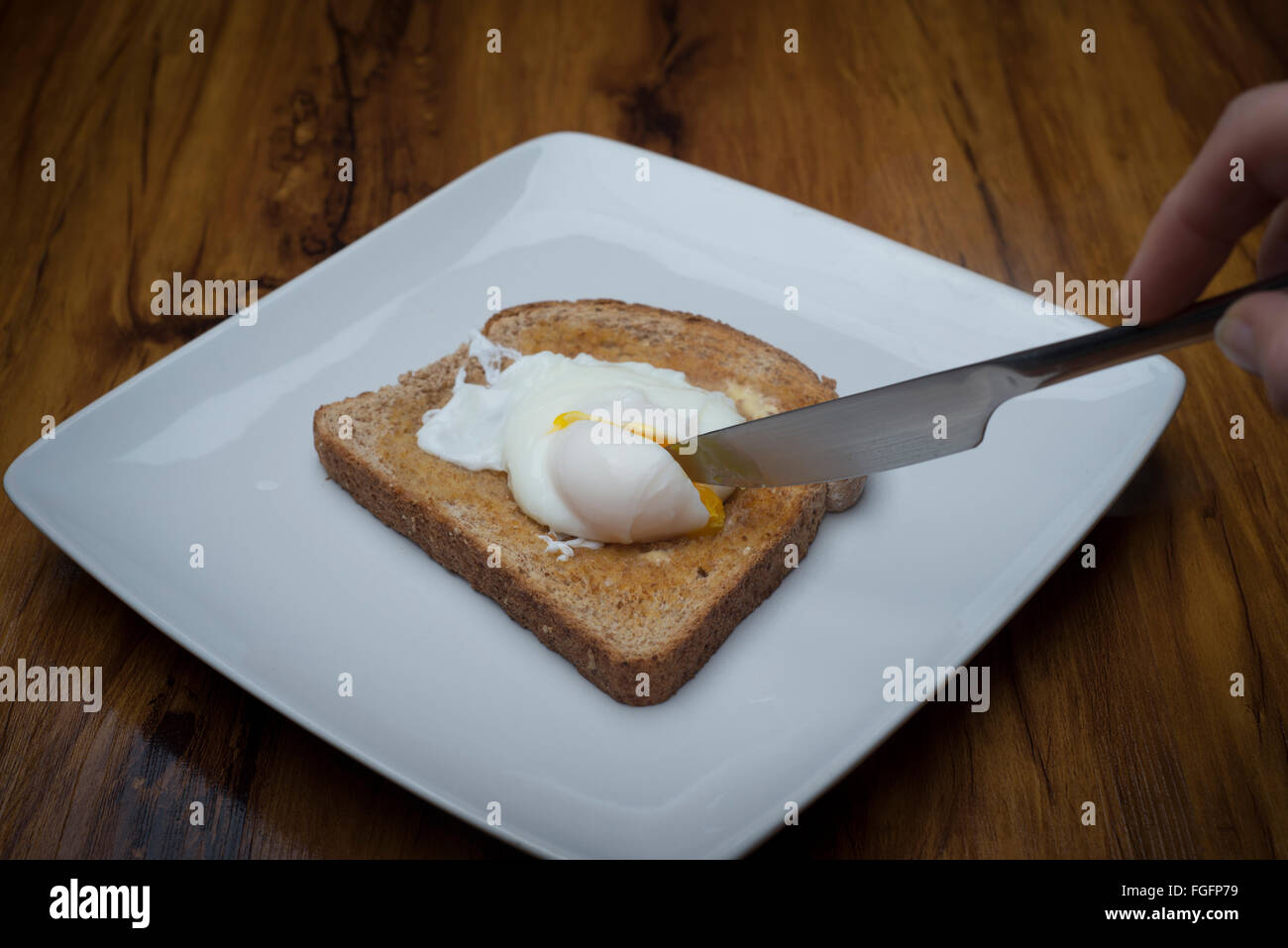 a knife cutting into a poached egg on toast Stock Photo