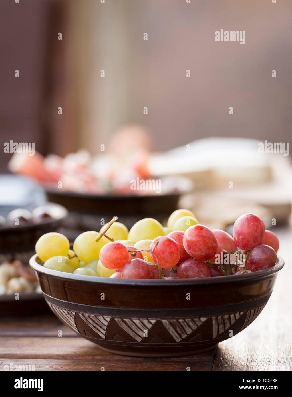 Classic antipasto food typical of the Mediterranean including grapes, olives, salami in shallow focus Stock Photo