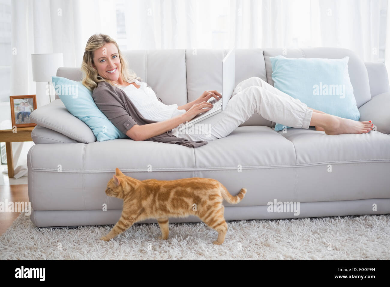 Woman lying on sofa using her laptop smiling at camera Stock Photo - Alamy
